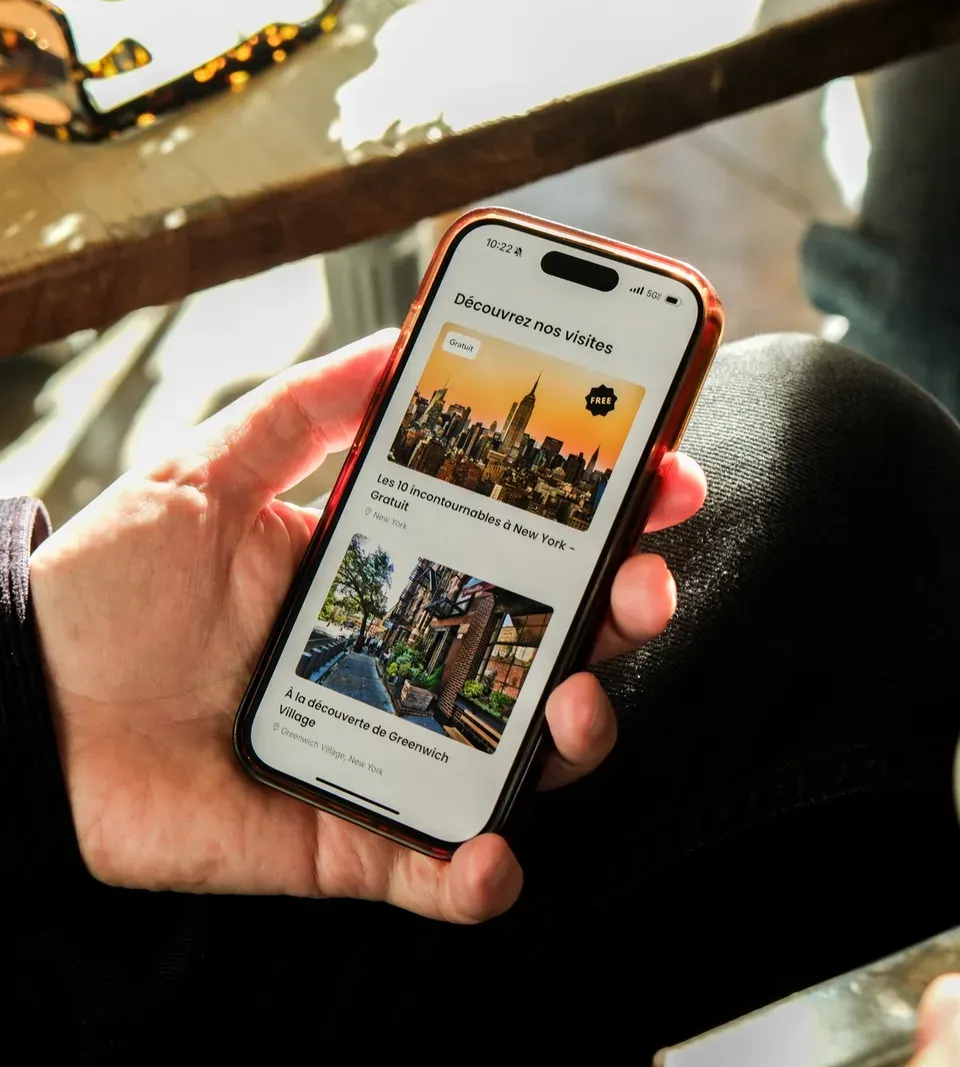 Une main tient un téléphone affichant le catalogue des balades Elya disponibles à New York.