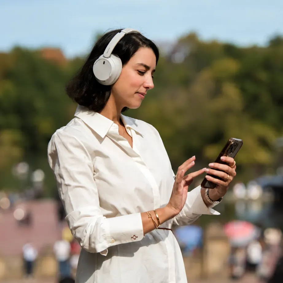 Une voyageuse écoute une balade Elya dans un parc, casque sur les oreilles.