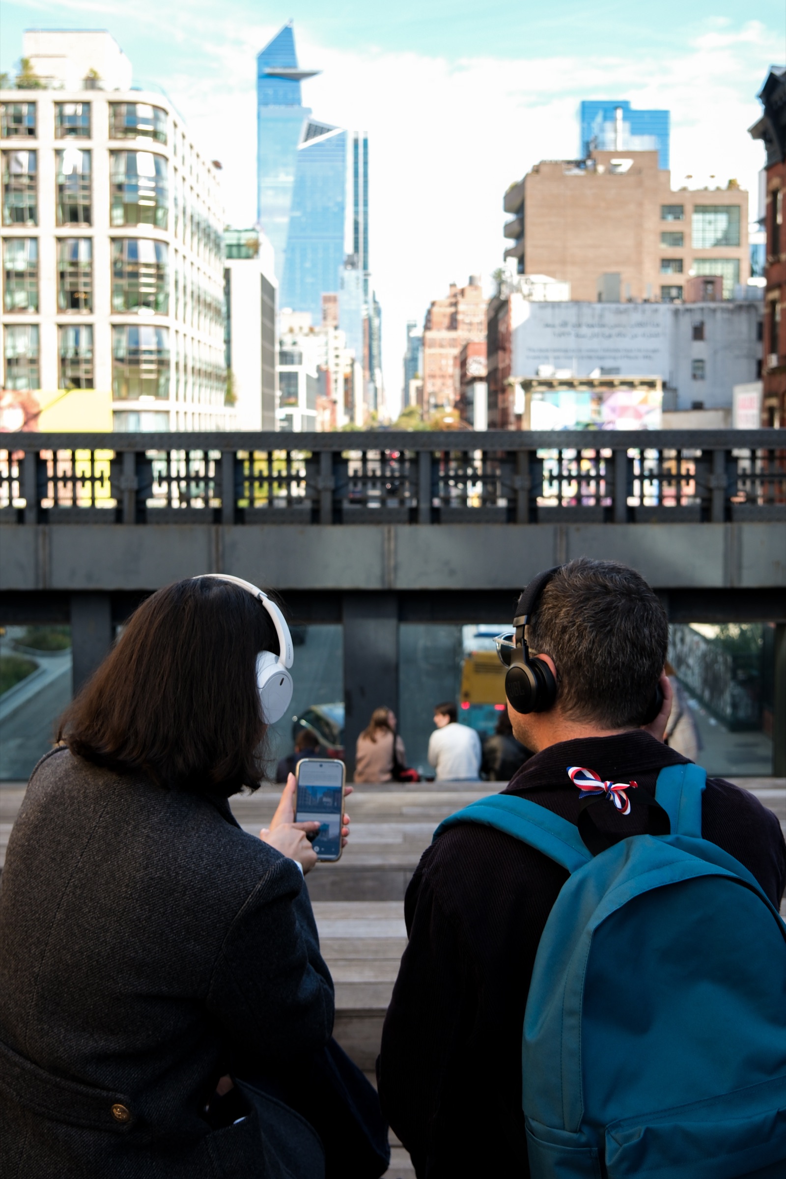 Un couple écoute Elya avec un casque, téléphone en main, face au skyline de New York depuis la High Line.